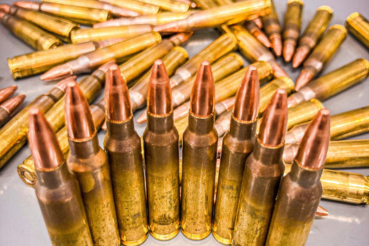 A collection of 5.56 caliber FMJ bullets with brass casing and copper tips, arranged in rows on a surface.